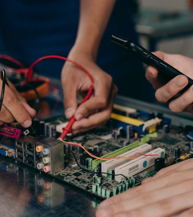 pexels-photo-9242887-9242887 Close-up of hands working on a motherboard using electrical tools and tester.